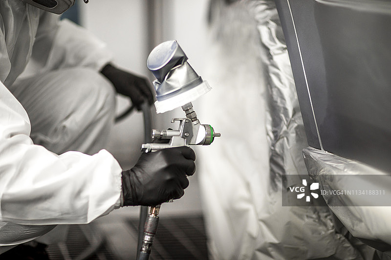 在车身修理厂的喷漆室用喷枪喷涂汽车部件图片素材