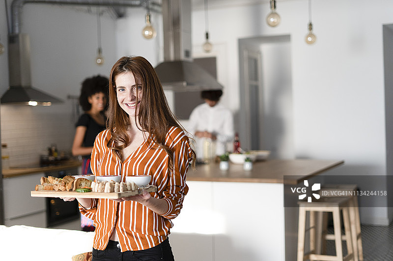 朋友们在厨房准备晚宴，女人 serving 开胃菜图片素材