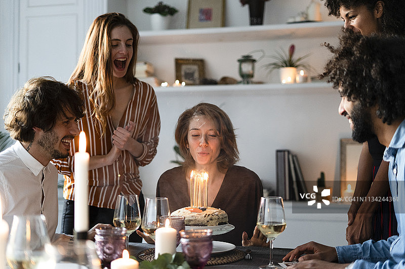 朋友们用点燃的生日蛋糕给年轻女子一个惊喜图片素材