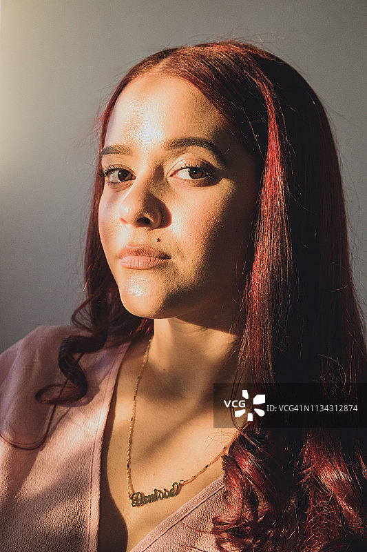 看着镜头的年轻拉丁裔女子肖像，未微笑。女子有红色头发，嘴边有一颗痣图片素材