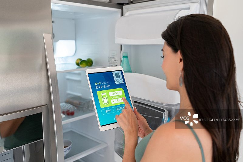女子使用平板电脑在家中控制冰箱图片素材