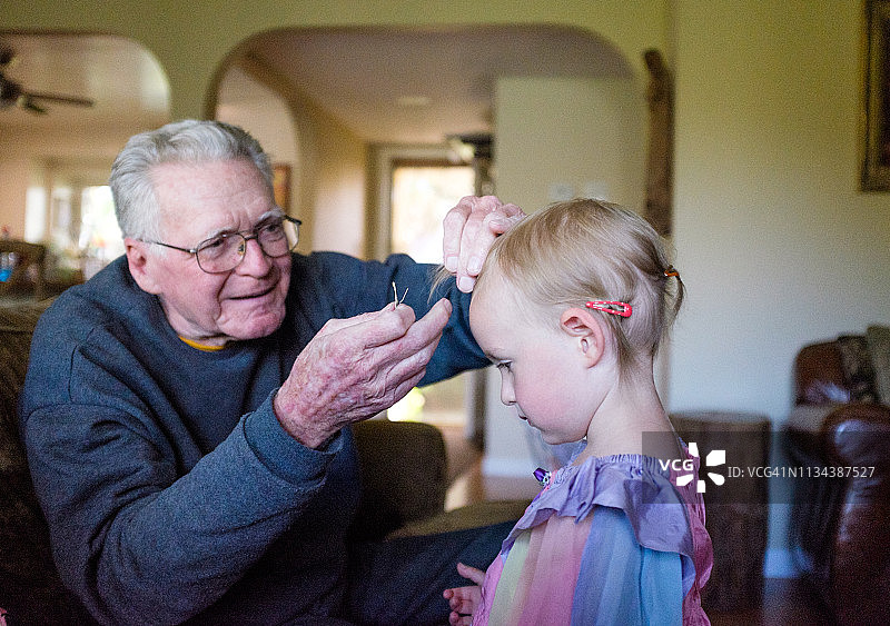 年长的祖父帮助他的小孙女把发夹夹到头发上图片素材