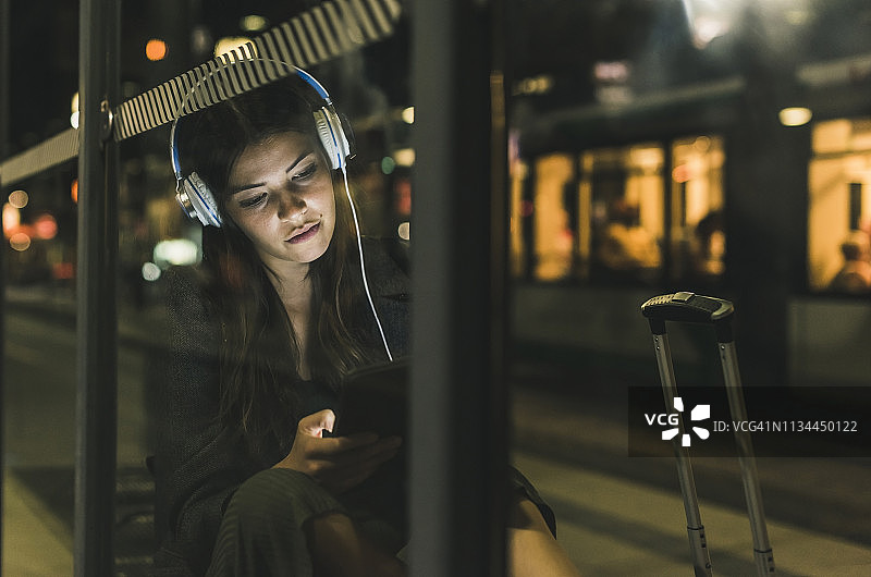 夜晚在车站戴耳机用平板电脑的年轻女人肖像图片素材