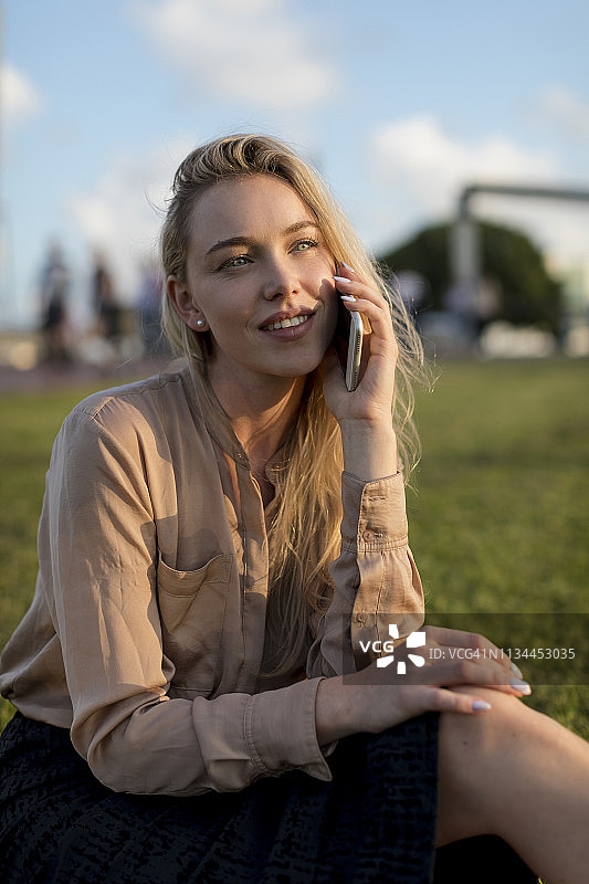在草地上用手机微笑的年轻女商人图片素材