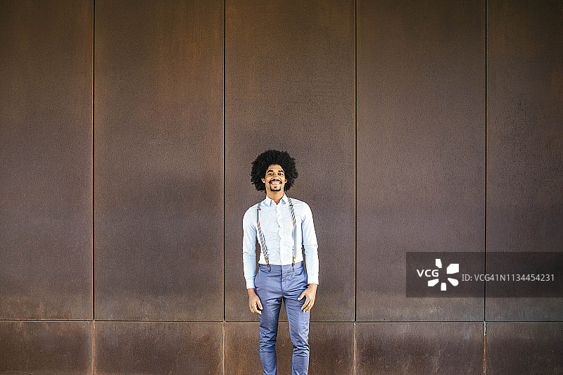 面带微笑的男人穿着吊带站在生锈的背景前的肖像图片素材