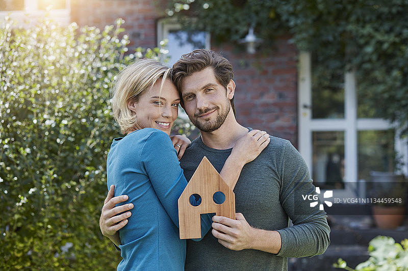 在自家房子前拿着房屋模型的幸福情侣肖像图片素材