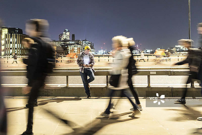 英国伦敦，男人看着手机，人行道上的人模糊不清图片素材