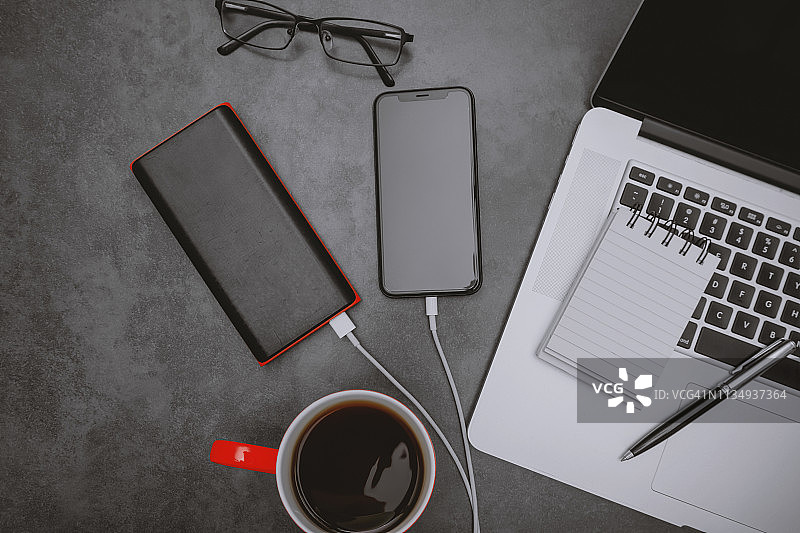 笔记本电脑、手机通过充电宝和咖啡杯在工作桌上充电图片素材
