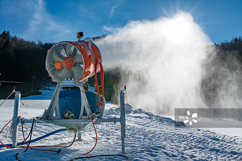 阳光明媚的滑雪坡上人工造雪机正在喷雪图片素材