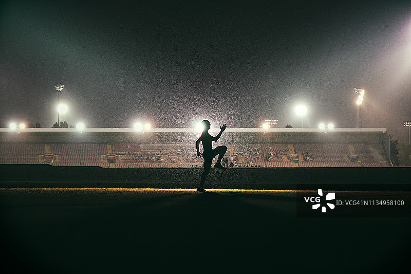 年轻运动员在体育场泛光灯前热身跑步图片素材