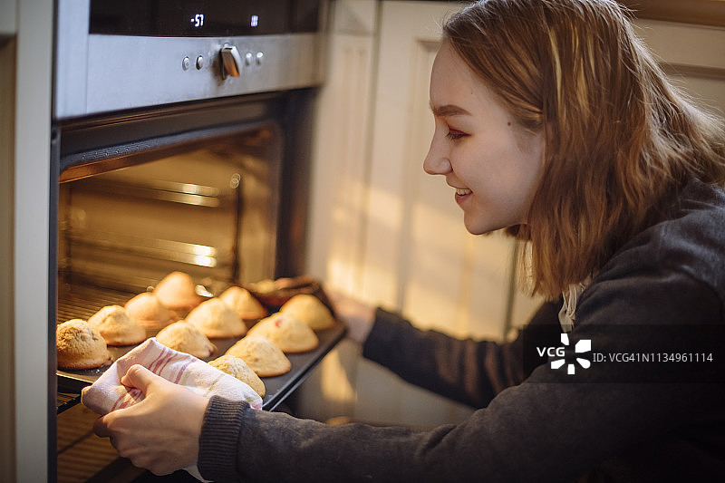 快乐女孩在厨房从烤箱中取出蛋糕图片素材