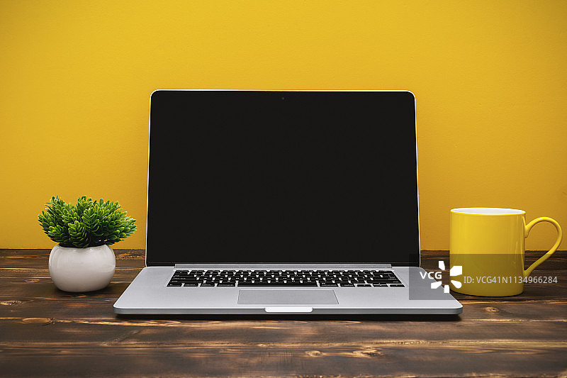 黄色背景下办公室桌子上的笔记本电脑和黄色咖啡杯图片素材