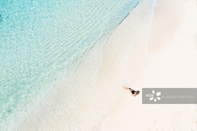 巴厘岛：年轻女子在白色沙滩上享受日光浴，透明的碧绿海水，航拍图片素材