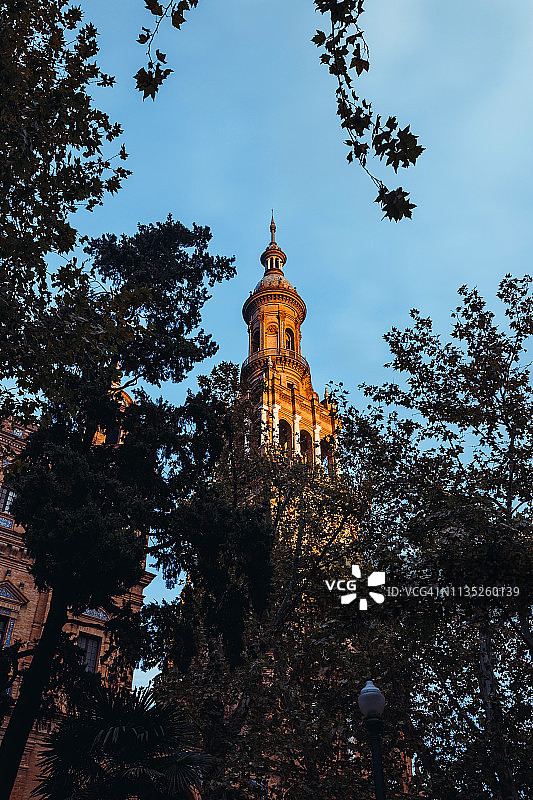西班牙广场的一座塔楼，在日落的光线下，从玛丽亚·路易莎公园的树丛中望去。西班牙塞维利亚，安达卢西亚，欧洲图片素材