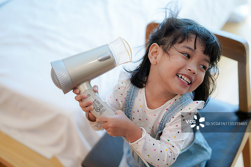 儿童活动概念：小女孩洗澡后用卷发器或吹风机吹干头发图片素材