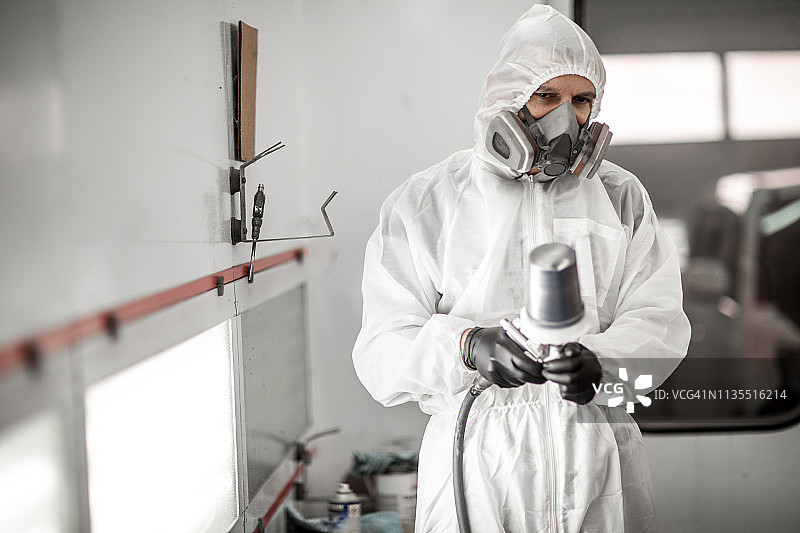 穿白色工作服和呼吸面罩的专业汽车喷漆工在喷漆房手持喷枪图片素材