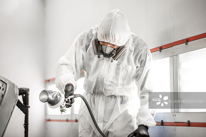 白色防护服的汽车调色师在车身车间的喷漆房中喷涂汽车零件图片素材