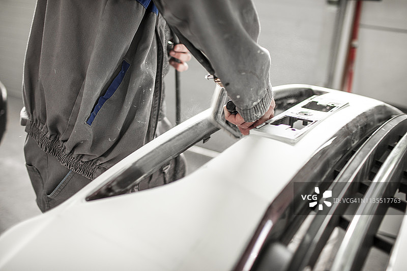 汽车维修技师使用打磨机去除汽车保险杠上多余的填充物图片素材