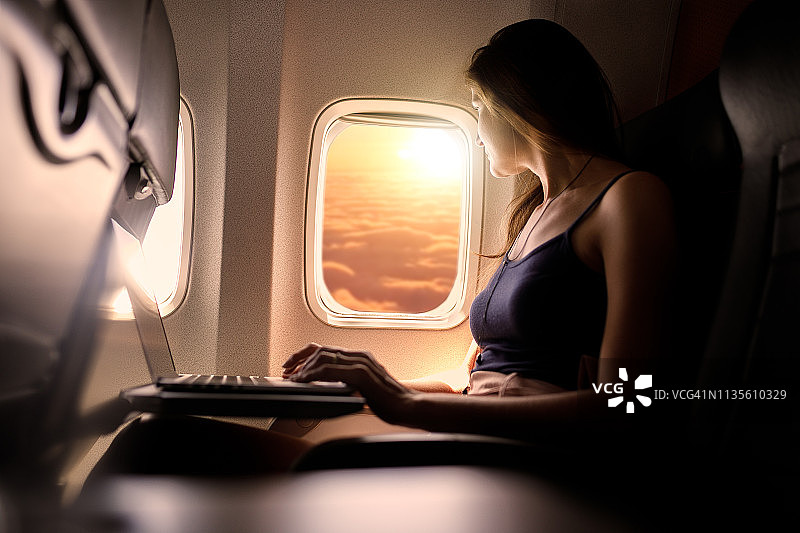 在飞机座位上使用笔记本电脑的女人图片素材