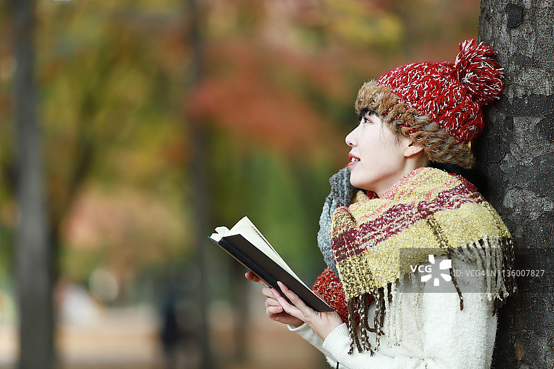 在秋季公园里看书的年轻女子图片素材