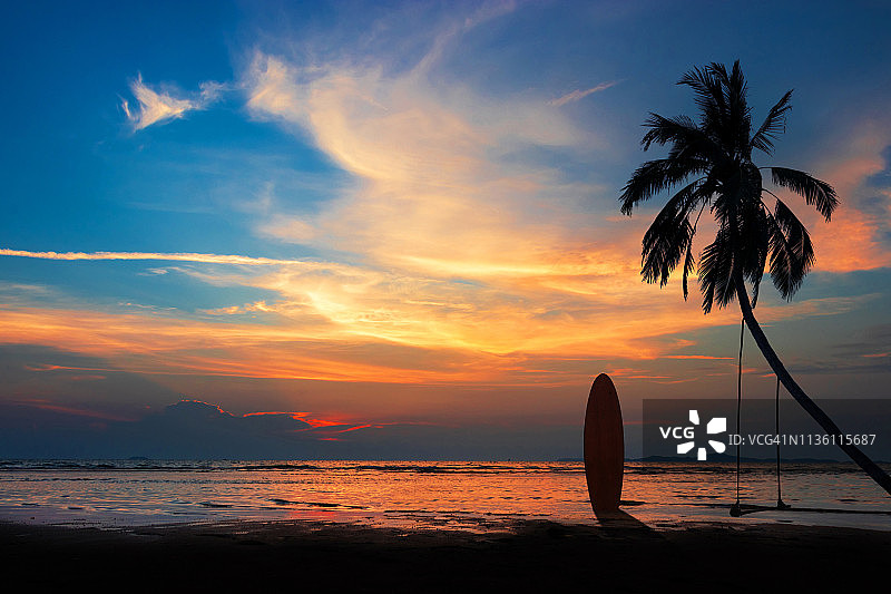 日落时分海滩上的冲浪板和椰子树剪影，天空色彩斑斓图片素材