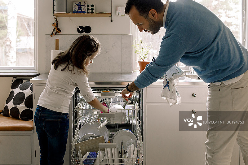 父女在厨房里整理洗碗机中的餐具图片素材
