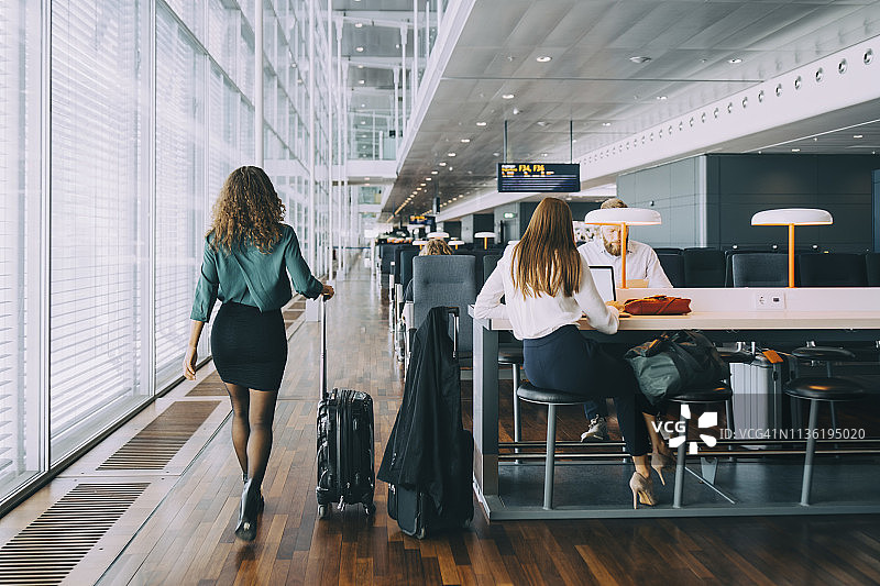商务女性在机场出发区与等待的同事一起拉着行李行走的全身后视图图片素材