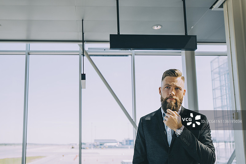 沉思的商人站在机场的窗户前图片素材