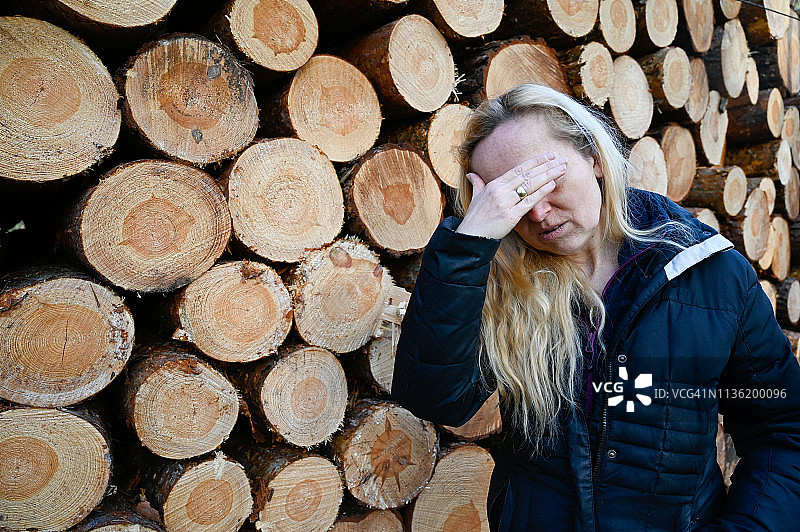 头痛的女人，背景是一些被砍伐的树干图片素材