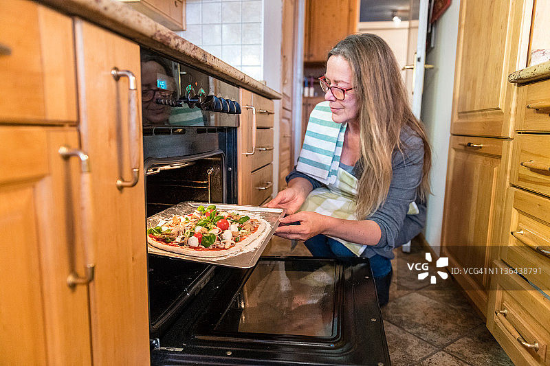 年长女人将素食披萨放入烤箱图片素材