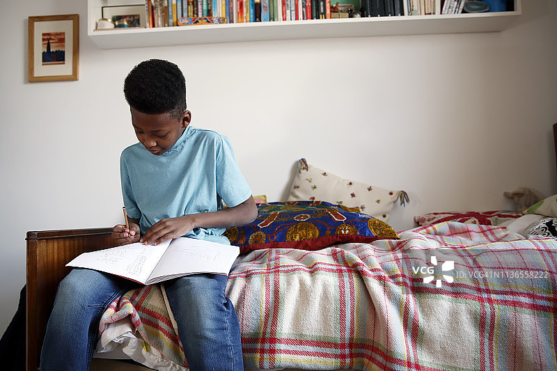 男孩坐在床角完成家庭作业图片素材
