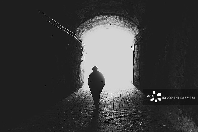 老年男子走向隧道尽头光亮的背影图片素材