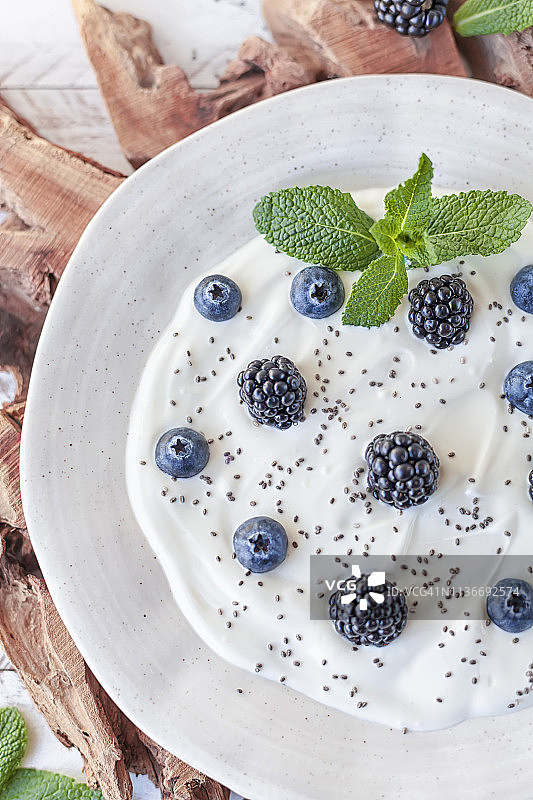 素食希腊酸奶，黑莓蓝莓奇亚籽，白色木桌。图片素材