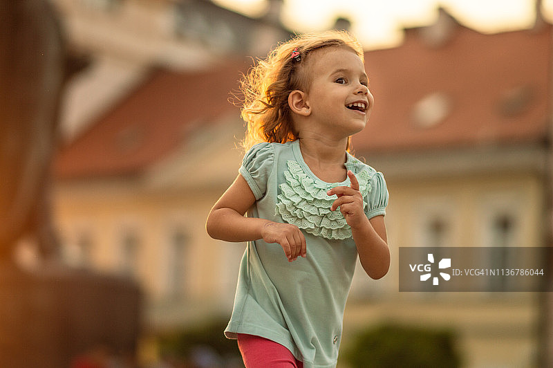 快乐的小女孩在金色日落的城市里奔跑图片素材