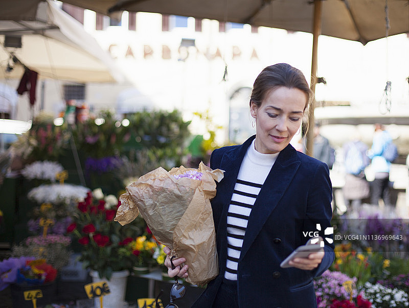 在花卉市场手捧盆栽使用智能手机的女人图片素材
