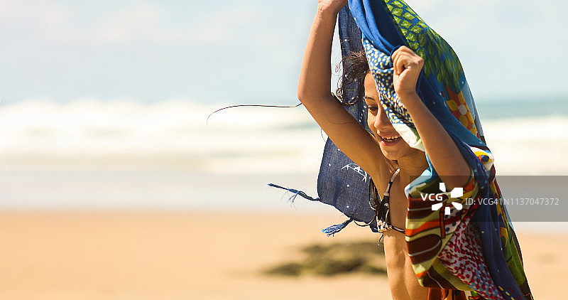 在海滩上拿着沙滩巾的年轻漂亮女孩图片素材