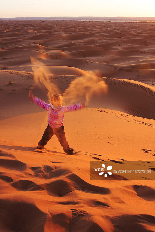 日落时分，小女孩扬起沙子，形成X形图片素材