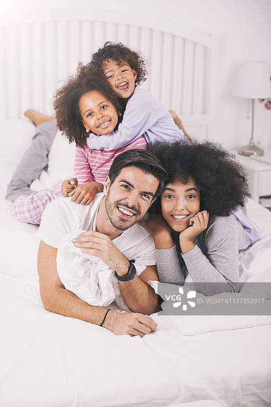 快乐的混血家庭躺在床上看着镜头图片素材