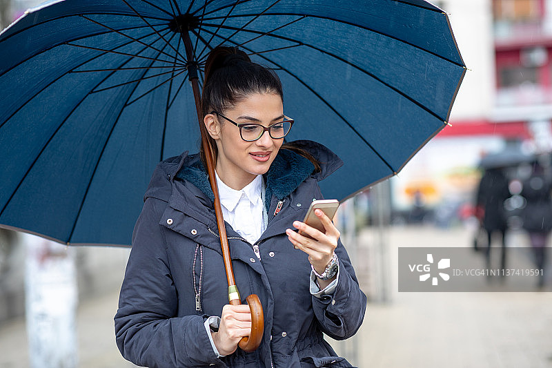 美丽的年轻女商务人士在打电话，同时拿着雨伞图片素材