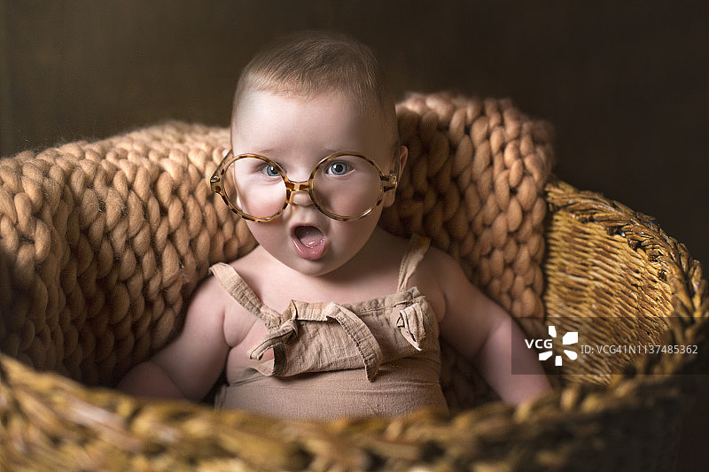 戴眼镜坐在篮子里的可爱有趣婴儿图片素材