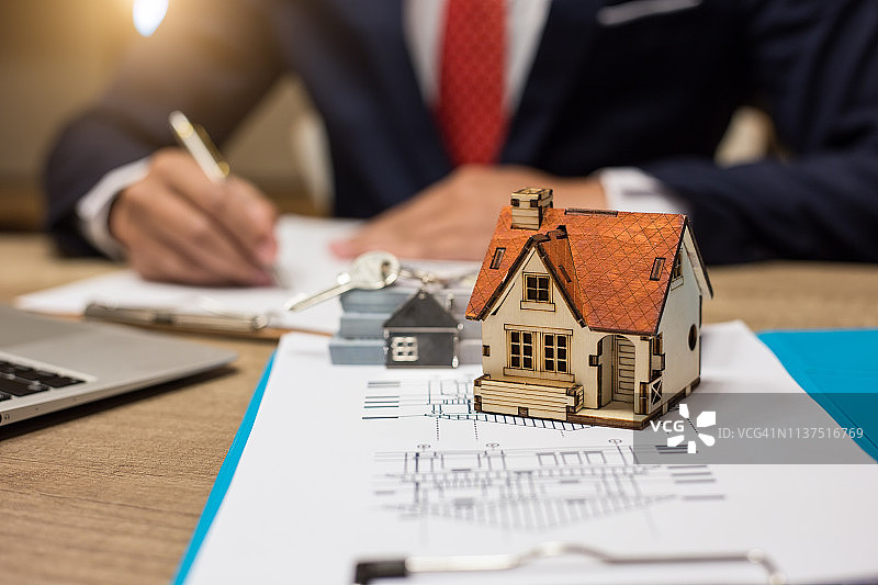商务人士在房屋建筑模型后签署合同图片素材