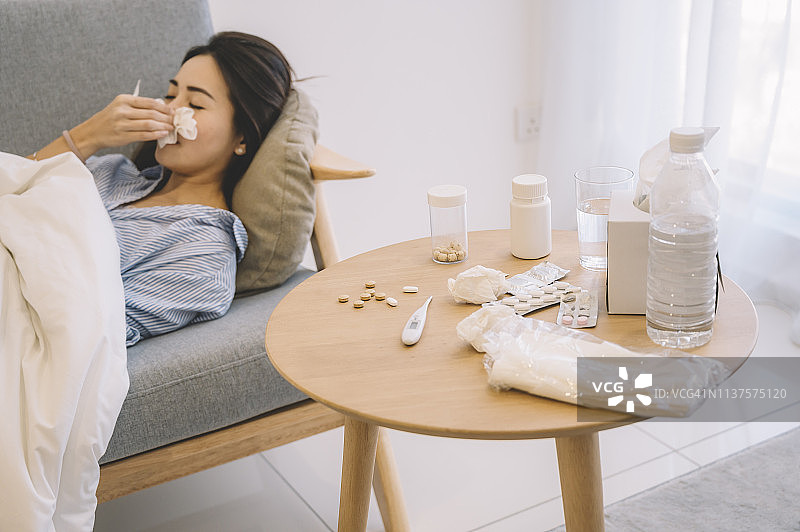 一位亚洲女人躺在客厅的沙发上，用纸巾捂住鼻子图片素材