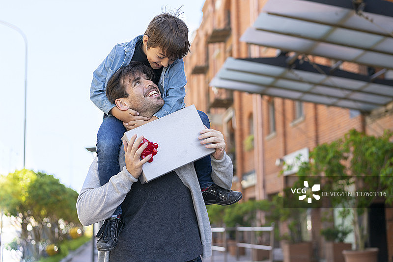 可爱的儿子在庆祝父亲节，给爸爸一个惊喜，爸爸把他扛在肩上，两人相视而笑图片素材