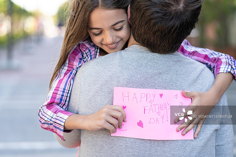 漂亮的女儿拿着父亲节卡片拥抱爸爸图片素材