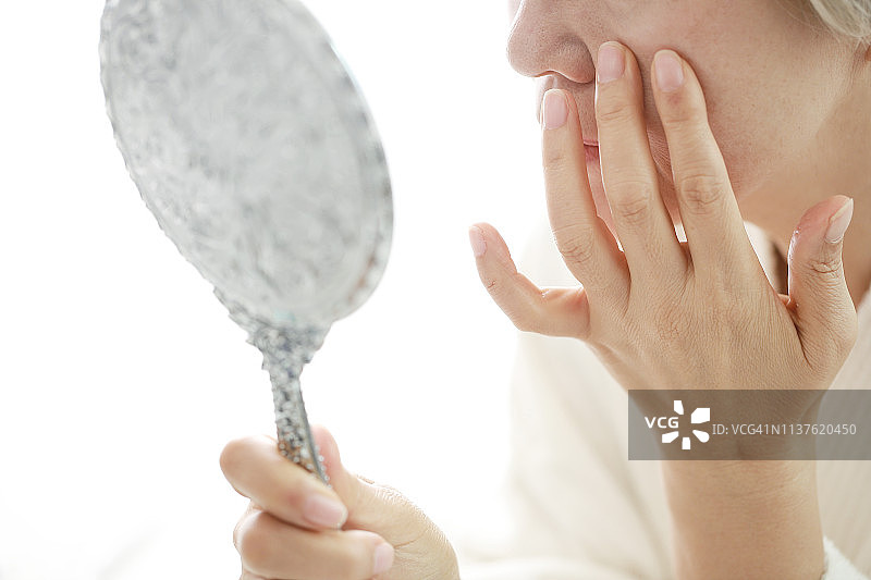 年长妇女检查皱纹的脸与镜子图片素材