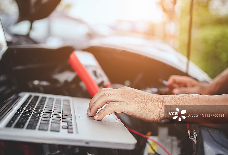 汽车修理工使用电脑和跨接启动汽车图片素材
