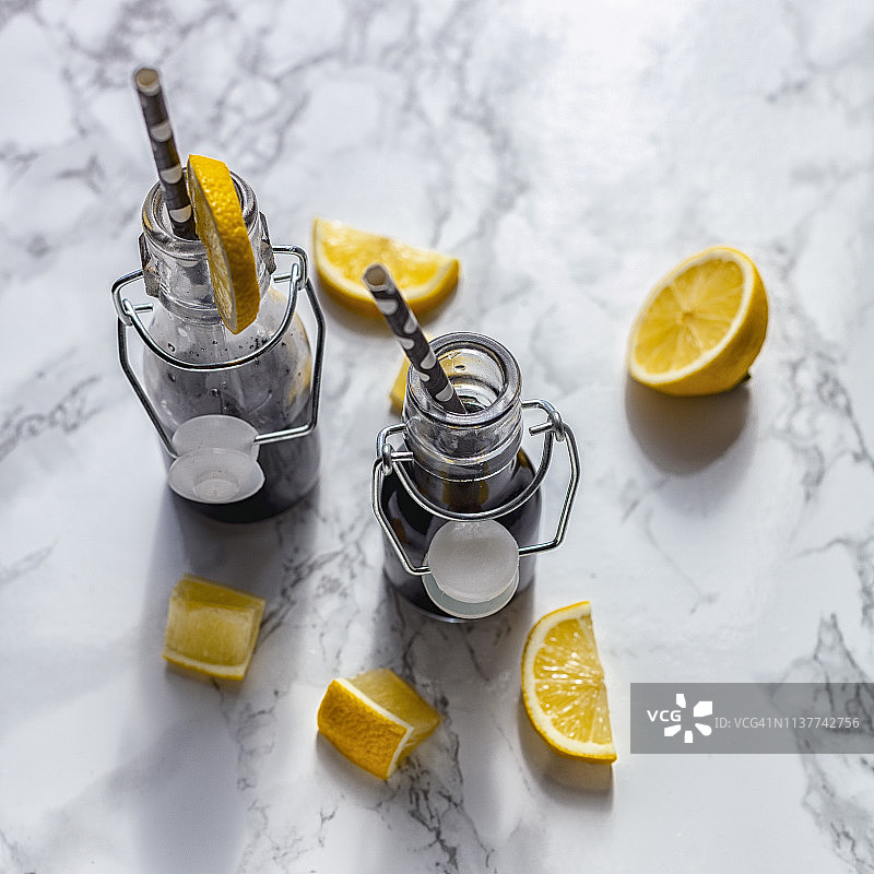 装在翻盖瓶中的活性炭排毒果汁或黑色柠檬水，配以椰子、青苹果和酸橙，白色大理石背景图片素材