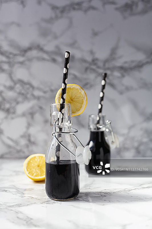 装在翻盖瓶中的活性炭排毒果汁或黑色柠檬水，配以椰子、青苹果和酸橙，白色大理石背景图片素材