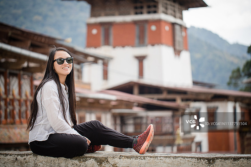 一位年轻女子坐在不丹特朗萨的壁架旁图片素材