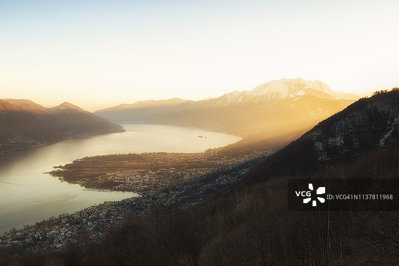 阳光照亮马焦雷湖和瑞士提契诺州的阿斯科纳和洛迦诺村庄图片素材